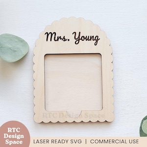 May include: A wooden frame with a scalloped edge and the text "Mrs. Young" engraved on the top. The frame has a cutout in the centre for a photo or other decorative element.