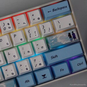 May include: A close-up of a mechanical keyboard with white and blue keycaps. The keycaps have Japanese characters and English labels. Some keys are light blue with a whale design. The Backspace key is light blue with the word "Backspace".