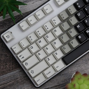 May include: A white mechanical keyboard with black keys for the function keys and arrow keys. The keyboard has a black frame and a white background.