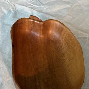 May include: A wooden bowl shaped like a heart. The bowl is made of light brown wood and has a smooth, polished finish.
