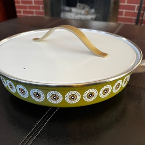 Könnte beinhalten: Ein grüner Emaille-Topf mit einem weißen Deckel und einem goldenen Griff. Der Topf hat ein weißes und goldenes geometrisches Muster am Rand.