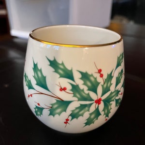 Puede incluir: Taza de cerámica blanca con borde dorado y diseño de hojas de acebo verdes y bayas rojas.