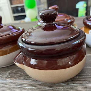 Puede incluir: Conjunto de cuatro tarros de cerámica marrón y blanco con tapas. Los tarros están esmaltados y tienen un aspecto rústico.