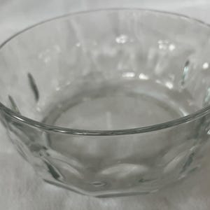 Może przedstawiać: Biały ceramiczny kubek z czarnym uchem i napisem "But First, Coffee" pogrubioną czcionką. Kubek jest ustawiony na rozmytym tle, sugerującym przytulne otoczenie.