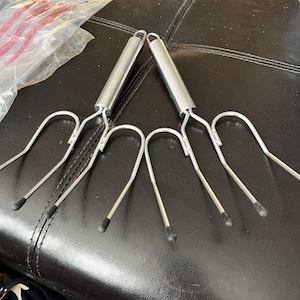 May include: Two silver grilling forks with black handles. The forks have three prongs each and are designed for grilling.