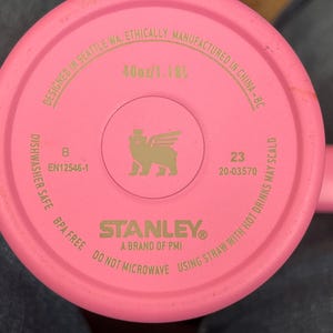 May include: A pink Stanley brand tumbler base with the text "40oz/1.18L". The base includes the text "Designed in Seattle WA, Ethically Manufactured in China-BC". The base also includes the text "Dishwasher Safe BPA Free Do Not Microwave Using Straw With Hot Drinks May Scald".