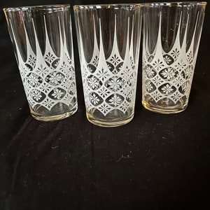 Puede incluir: Tres vasos de beber de vidrio transparente con un patrón geométrico grabado en blanco. El patrón presenta un diseño repetitivo de diamantes y estrellas.