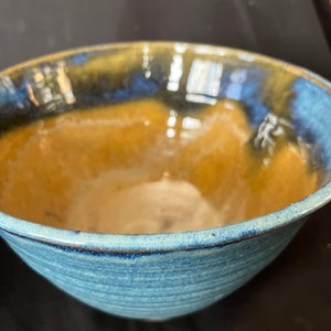 May include: A blue and brown ceramic bowl with a glazed finish. The bowl has a rounded shape and a slightly flared rim.