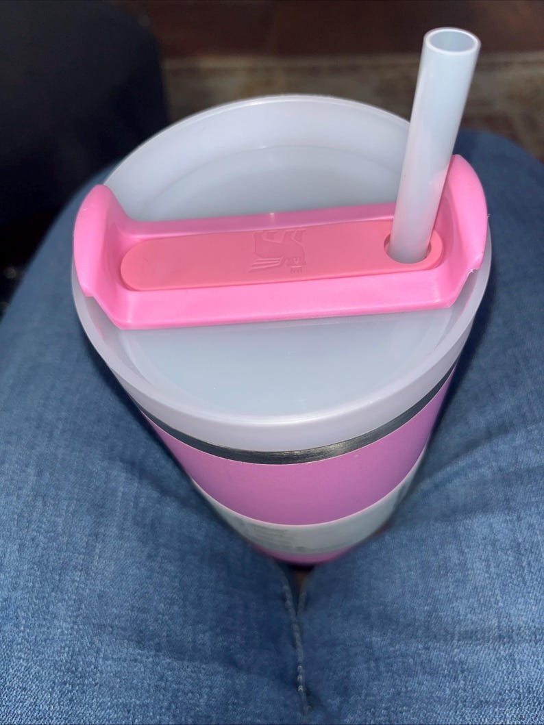 May include: A pink and white insulated tumbler with a clear lid and a pink handle. A white straw is inserted into the lid. The tumbler has a pink band around the middle and a silver band below it.