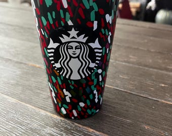 May include: A black and green reusable travel mug with a white Starbucks logo and a confetti-like pattern. The mug has a green lid.