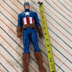 May include: A blue and red Captain America action figure with a brown belt and boots. The figure is 11 inches tall.
