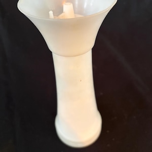 May include: A white plastic funnel-shaped object with a cylindrical base and a wide, flared top opening. The interior of the flared section features a small, central nozzle-like protrusion extending upward from the bottom of the basin.