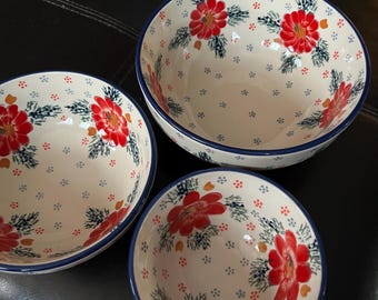 Pode incluir: Três tigelas de cerâmica com um design floral. As tigelas são brancas com flores vermelhas e folhas verdes. As tigelas têm uma borda azul.