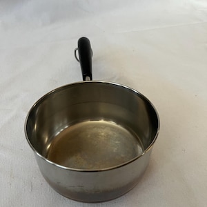 May include: A stainless steel saucepan with a black handle. The small pot has a rounded body and a single, long handle. The interior of the pan is visible, and the handle is attached with a metal loop.