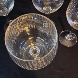 May include: A collection of clear glass stemware, including wine glasses and a large bowl. The bowl has a textured, ribbed design. The glasses are arranged against a dark background, reflecting light.