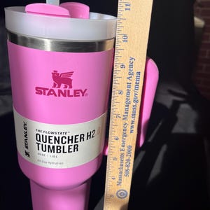 May include: A pink Stanley Quencher H2.0 tumbler with a white lid and a handle. The tumbler has the Stanley logo and the text "QUENCHER H2.0 TUMBLER" on the side. It holds 1.18L and is approximately 28 cm tall.