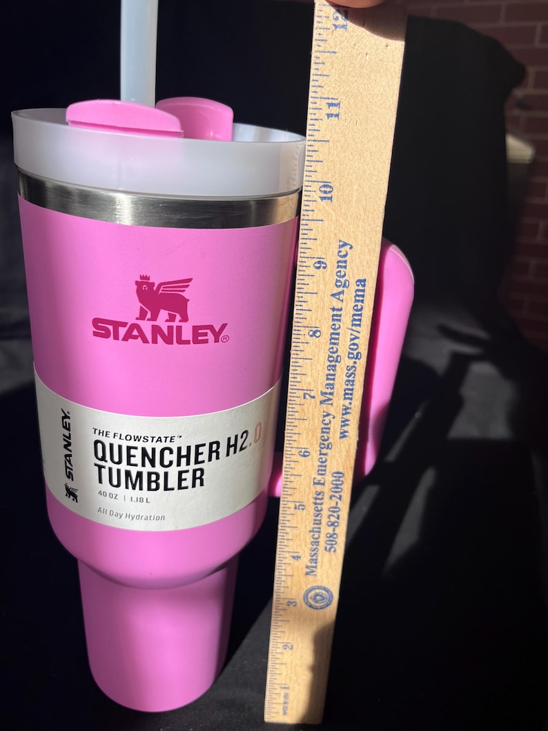 May include: A pink Stanley Quencher H2.0 tumbler with a white lid and a handle. The tumbler has the Stanley logo and the text "QUENCHER H2.0 TUMBLER" on the side. It holds 1.18L and is approximately 28 cm tall.
