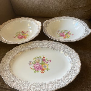 Puede incluir: Tres platos de cerámica blanca con ribetes dorados y diseños florales. Los platos son una fuente para servir y dos tazones.