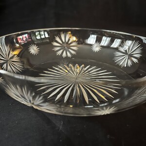 May include: A clear glass bowl with a starburst pattern etched into the bottom and sides. The bowl is empty and sitting on a black surface.