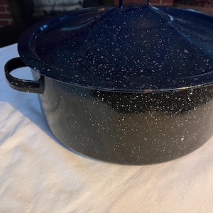 May include: A large, speckled black and navy blue enamelware pot with a matching lid. The pot has two side handles and a handle on the lid. The pot is sitting on a white surface.