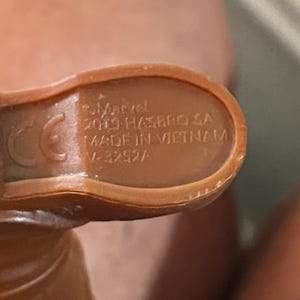 May include: Close-up of the bottom of a brown plastic toy figure. The figure has a CE mark and the text "Marvel 2019 Hasbro SA Made in Vietnam V-3252A".