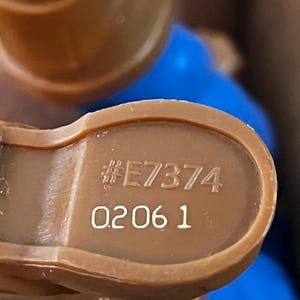 May include: Close-up of a brown plastic toy with the number "#E7374" and "0206 1" printed on it.