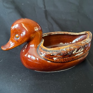以下が含まれることがあります： 釉薬仕上げの茶色のセラミック製の鴨のプランター。鴨は背中に詳細なデザインが施され、植えるための小さな開口部があります。