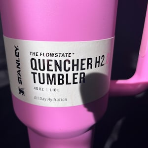 May include: A pink Stanley Quencher H2.0 Tumbler with a handle. The tumbler has the Stanley logo and the text "THE FLOWSTATE QUENCHER H2.0 TUMBLER 1.18 L All Day Hydration" printed on it.
