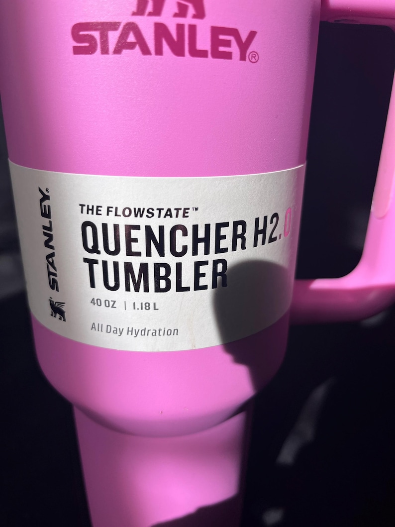 May include: A pink Stanley Quencher H2.0 Tumbler with a handle. The tumbler has the Stanley logo and the text "THE FLOWSTATE QUENCHER H2.0 TUMBLER 1.18 L All Day Hydration" printed on it.