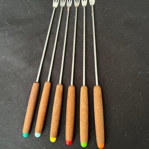 Può includere: Set di sei forchette per fondue con manici in legno. I manici sono dipinti in diversi colori: verde, blu, giallo, arancione, rosso e arancione.