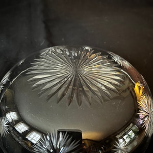 May include: A clear glass bowl with a starburst pattern etched into the bottom. The bowl is reflecting light from a window.