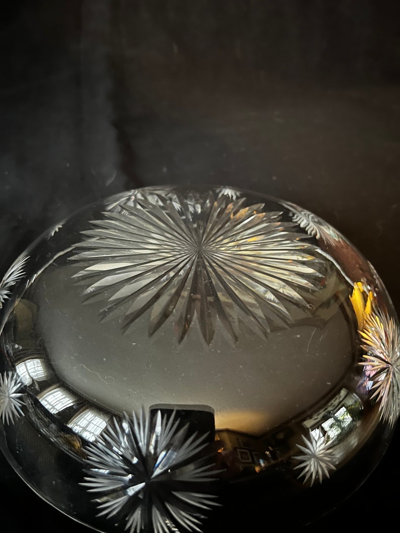 May include: A clear glass bowl with a starburst pattern etched into the bottom. The bowl is reflecting light from a window.