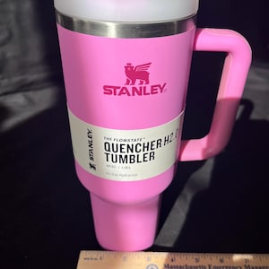 May include: A pink Stanley Quencher H2.0 tumbler with a handle, straw, and lid. The tumbler has the Stanley logo and text that reads "THE FLOWSTATE QUENCHER H2.0 TUMBLER 40 OZ | 1.18L All Day Hydration".