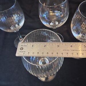 May include: Four clear wine glasses with a textured, ribbed design. The glasses are approximately 4 inches (10 cm) tall. The glasses are on a dark surface.