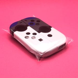May include: White and black Nintendo Switch Joy-Con shell with purple accents. The shell is made of plastic and has a textured surface.
