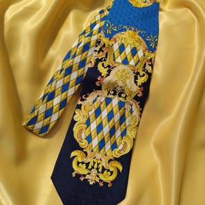 Puede incluir: Una corbata estampada con una base azul marino y un diseño de diamantes amarillos y blancos repetidos. La corbata también tiene una sección azul con un diseño dorado ornamentado.