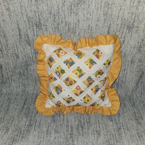 May include: A square throw pillow featuring a cathedral window quilt pattern with a yellow, blue, and white floral print fabric visible through the white lattice overlay. The pillow is finished with a solid mustard yellow ruffled border.