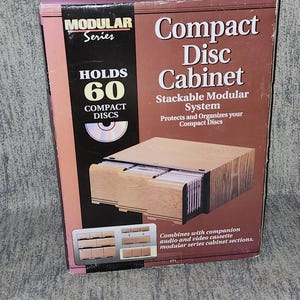May include: A brown and black cardboard box for a Modular Series Compact Disc Cabinet. The box features text stating it holds 60 compact discs, is a stackable modular system, and protects and organizes compact discs with images of the unit.