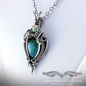 May include: A silver wire wrapped pendant featuring a green and blue gemstone with a smaller white opal gemstone above it. The pendant is attached to a silver chain.