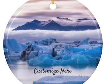 May include: Round ceramic ornament featuring a scenic landscape of blue icebergs and mountains under a cloudy sky. The ornament has a gold string for hanging and the text "Customize Here".