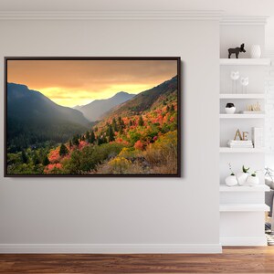 May include: A framed photograph of a mountain valley with a sunset in the background. The valley is covered in trees with fall foliage in shades of red, orange, and yellow.