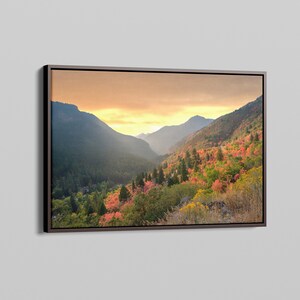 May include: A framed landscape photograph of a mountain valley with fall foliage in shades of red, orange, and yellow. The sky is a soft golden color, and the mountains are covered in trees.