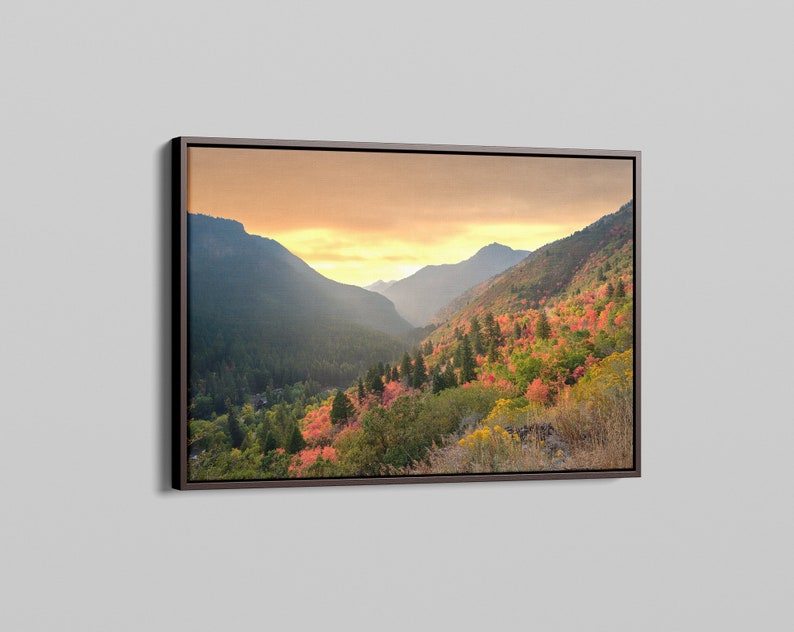 May include: A framed landscape photograph of a mountain valley with fall foliage in shades of red, orange, and yellow. The sky is a soft golden color, and the mountains are covered in trees.