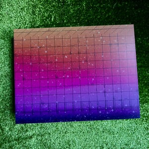 May include: A rectangular artwork with a gradient of colors, transitioning from brown to purple. The artwork features a grid pattern and small white star-like shapes. The piece is set against a green, textured background.