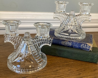 May include: Two clear glass candle holders with a geometric design. Each holder has three candle cups and a wide base.