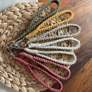 Op de afbeelding: Een set van zes kleurrijke macramé sleutelhangers met verschillende kleuren en patronen. De sleutelhangers zijn gemaakt van gevlochten koord en hebben een lus aan de bovenkant om sleutels aan te bevestigen.