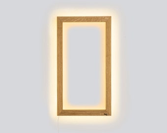 May include: A rectangular wooden frame with a warm white light illuminating the edges. The frame is mounted on a white wall with a white cord extending from the bottom.