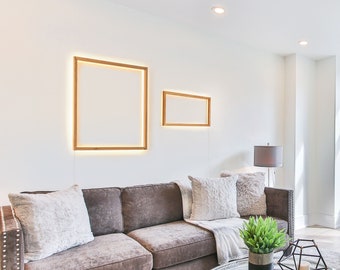 May include: A brown leather sofa with white pillows sits in a living room with a glass coffee table, a white armchair, and a potted plant. The room has white walls and a large window with a view of trees.