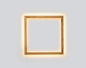 May include: A square wooden frame with a warm white light illuminating the edges. The frame is mounted on a white wall.
