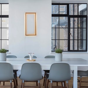 Può includere: Un tavolo bianco con sei sedie grigie, una pianta in vaso e un quadro incorniciato su una parete bianca. Il tavolo è apparecchiato con un vaso di matite e un vassoio di legno.